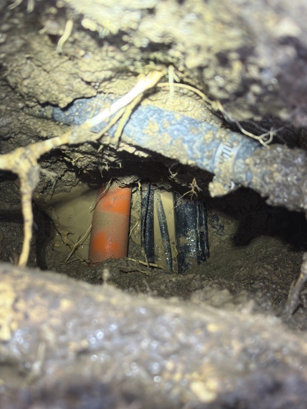 Close view of exposed orange conduit and cables in a test hole