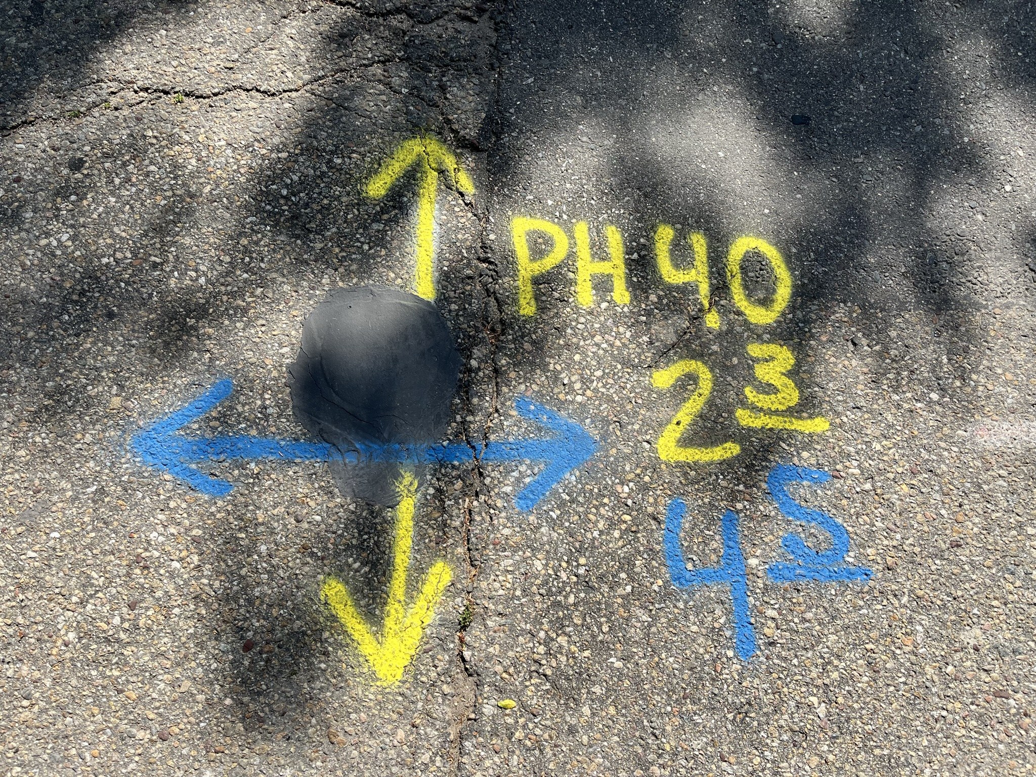 Yellow and blue paint marks on asphalt over a completed pothole