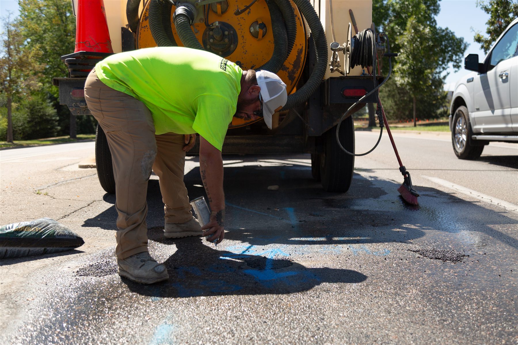 Crew spraying blue utility paint marks on asphalt after potholing