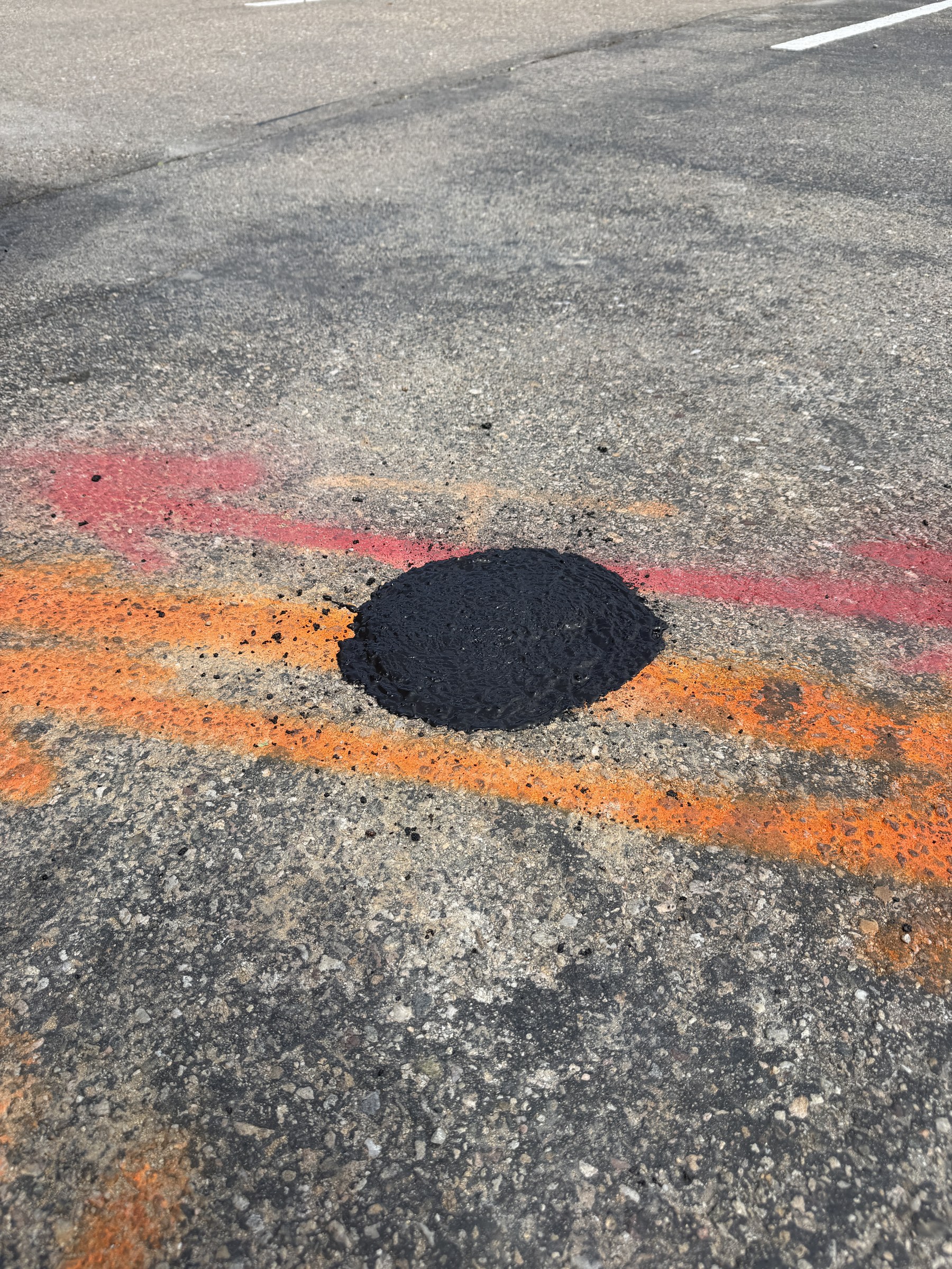Restored asphalt patch with orange and red utility marks